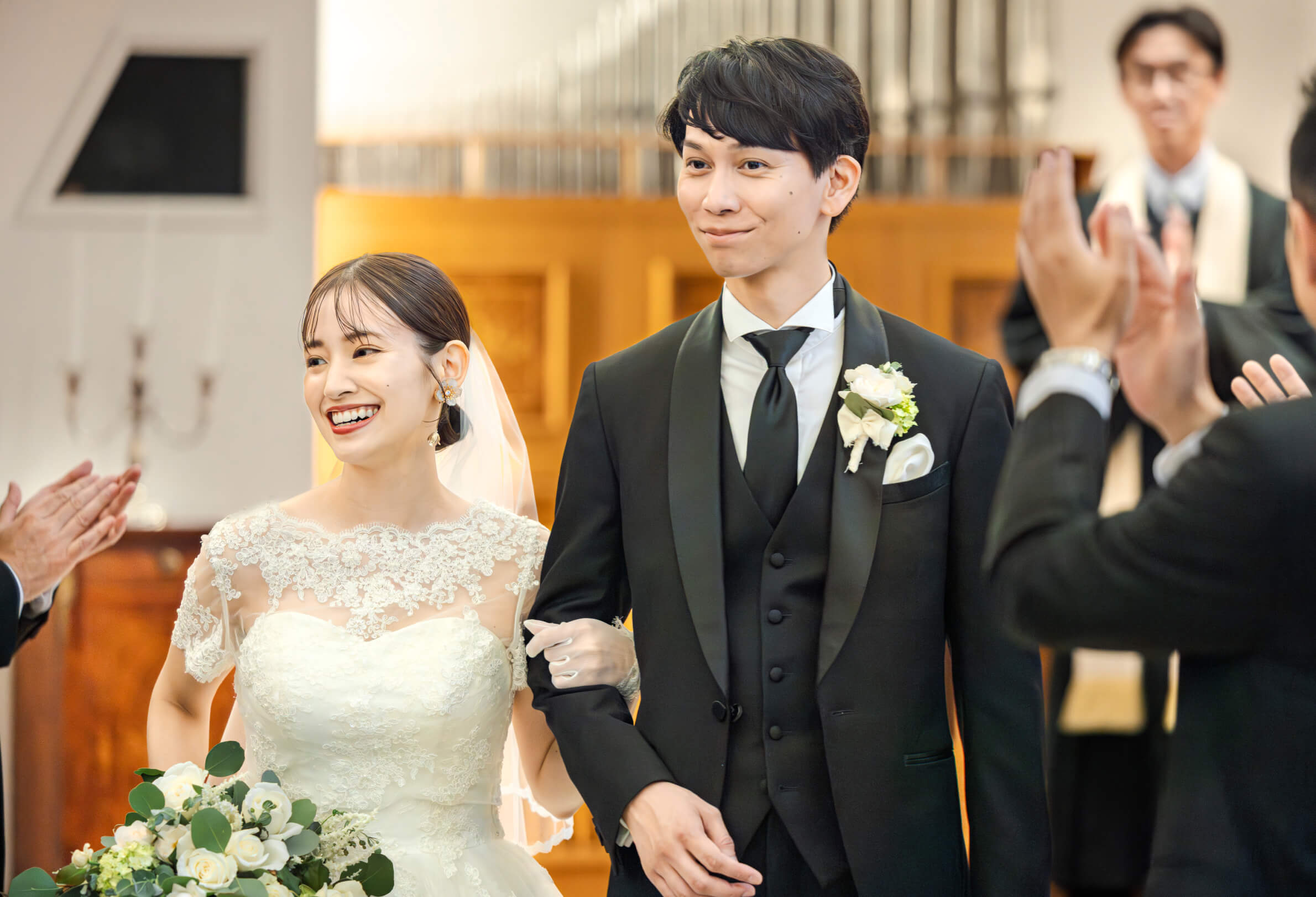 参列者の拍手に囲まれ笑顔を見せる新郎新婦
