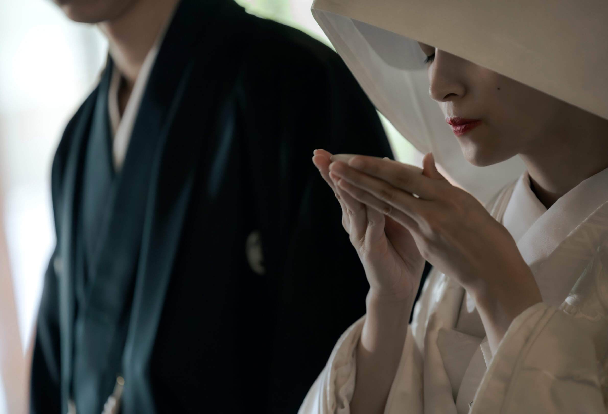 綿帽子姿で手を合わせる花嫁と紋付袴の新郎