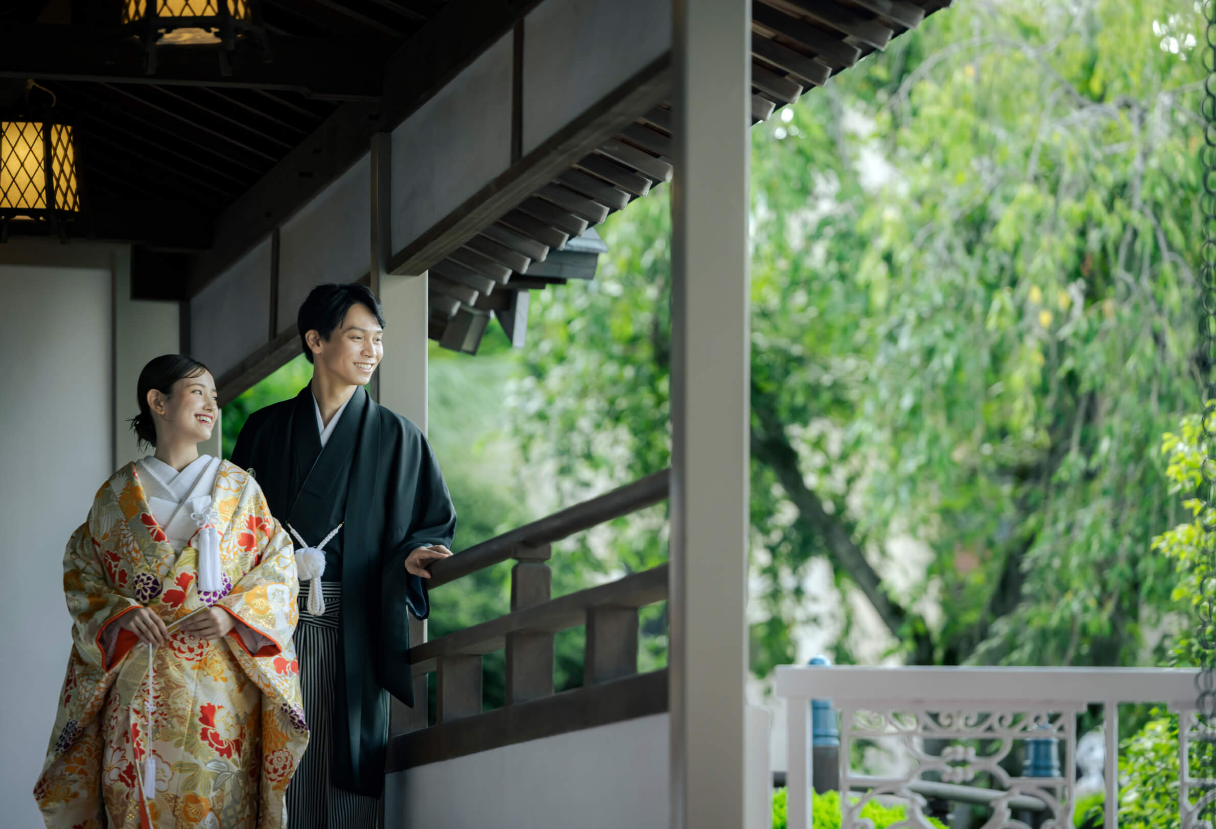 色打掛と羽織袴姿で庭園を望む廊下に立つ新郎新婦