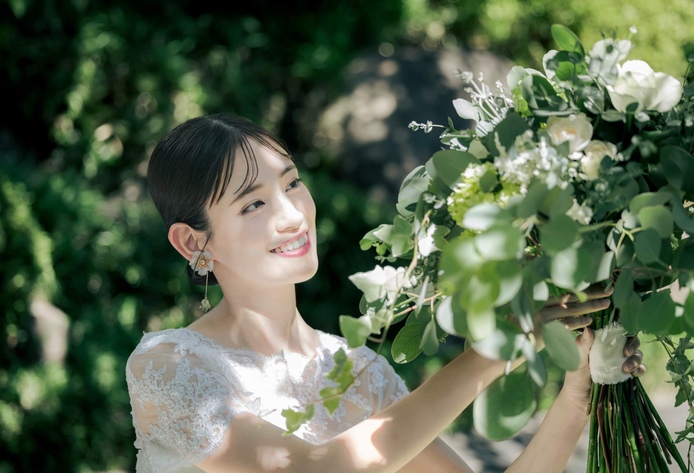 庭園の緑を背景にブーケを見つめる花嫁