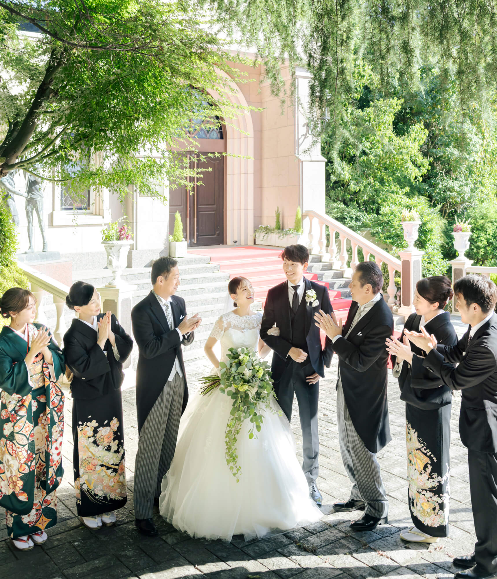 赤いカーペットの階段で家族に祝福される新郎新婦