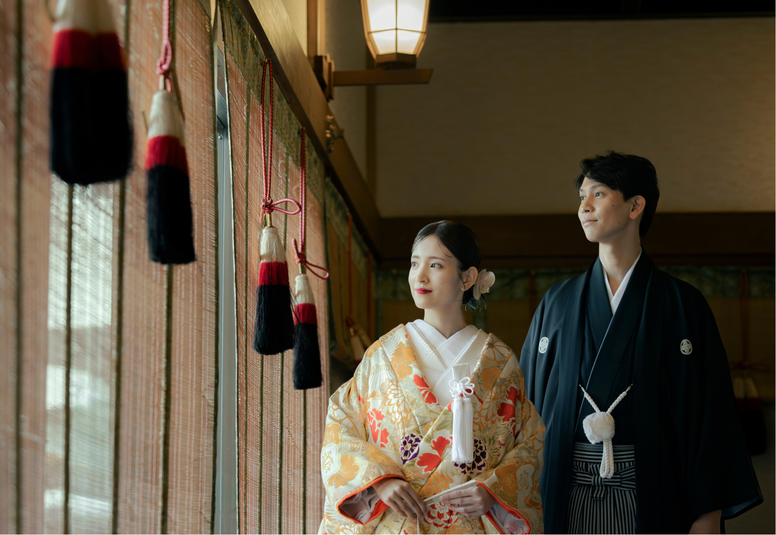 灯りに包まれた廊下に佇む色打掛と紋付袴姿の新郎新婦